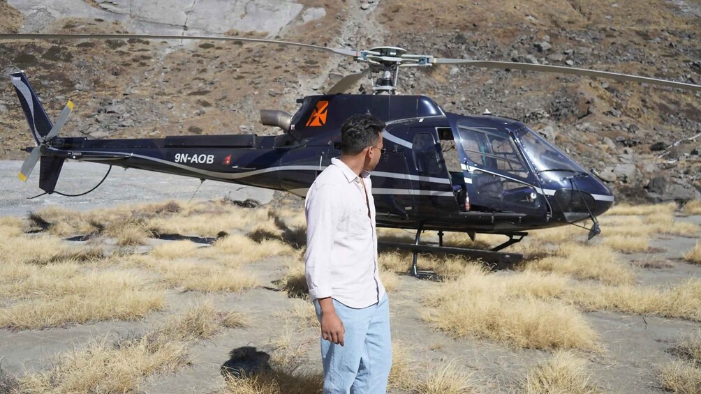A man standing in front of a helicopter with the registration number 9N-AOB. 5