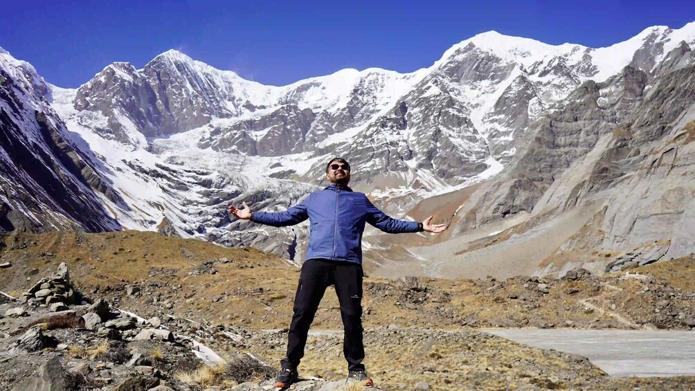 A person standing with arms outstretched in a mountainous landscape with snow-capped peaks. 4