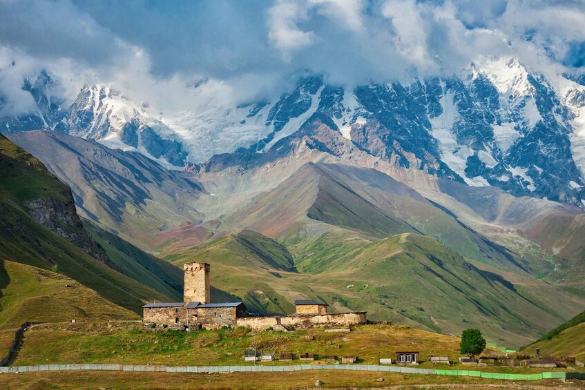 A historic stone building with a tower, surrounded by mountainous terrain and snow-capped peaks. 3
