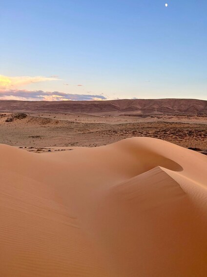 Sand dunes in a desert landscape with a clear sky and a crescent moon. 4