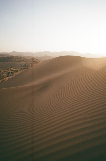 A vast desert landscape with undulating sand dunes and distant hills. 2