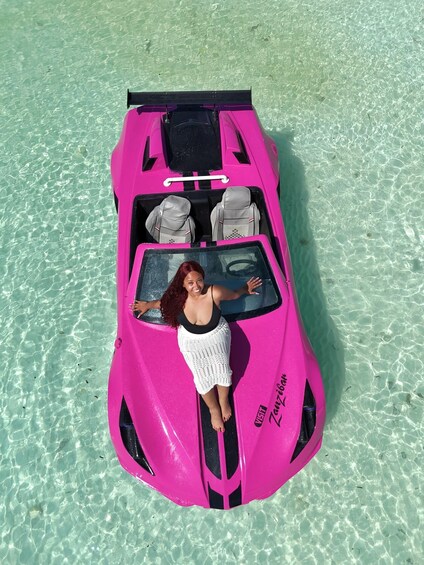 A pink convertible car with a woman sitting in the driver's seat on a beach. 3