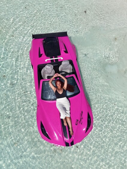 A person lying on a pink inflatable vehicle on a sandy beach with clear water. 4