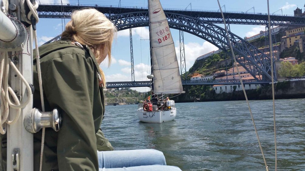 A person on a boat with a sail, a bridge in the background, and a cityscape with buildings. 5