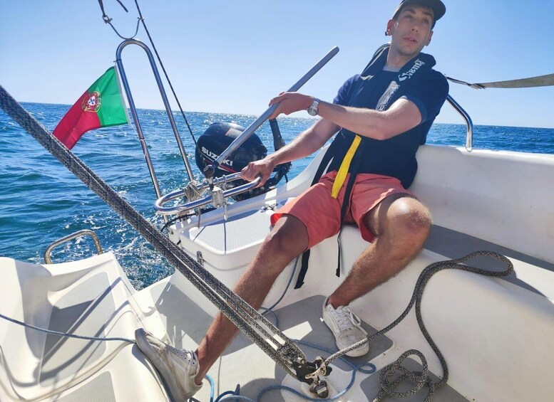 A person on a sailboat with a flag, steering wheel, and ropes. 1