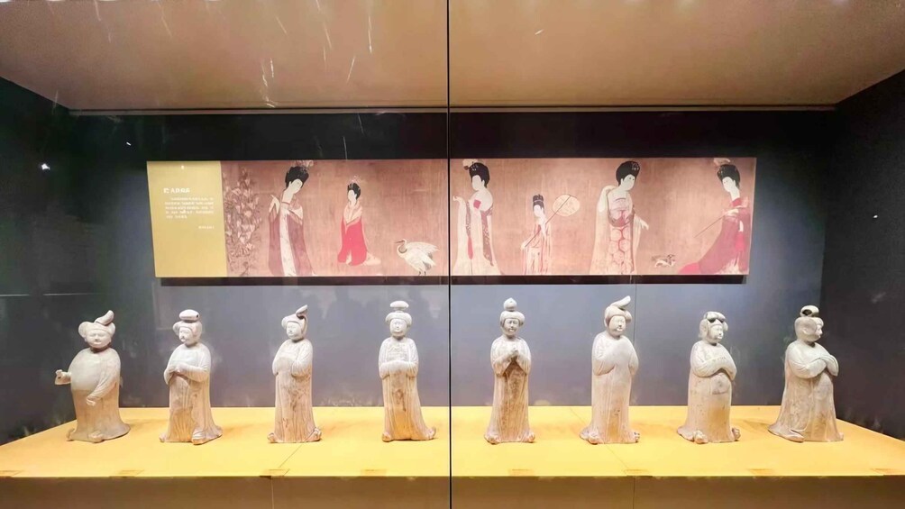 A museum display with ancient Chinese sculptures and a large painting above. 2