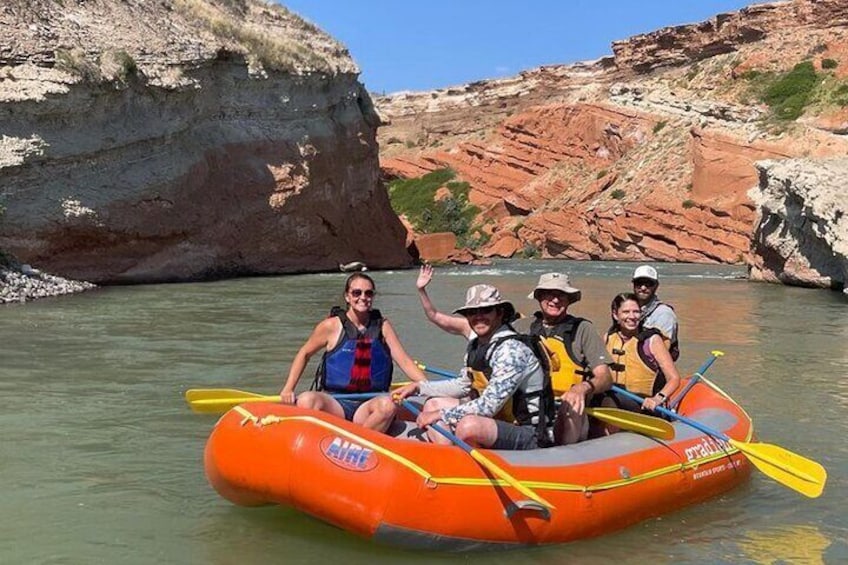 A group of people in an inflatable raft on a river surrounded by rocky cliffs. 1