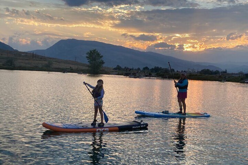 Two people paddleboarding on a calm lake with mountains in the background. 3