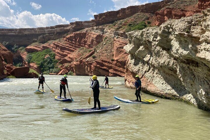 People paddleboarding on a river with red rock cliffs in the background. 5