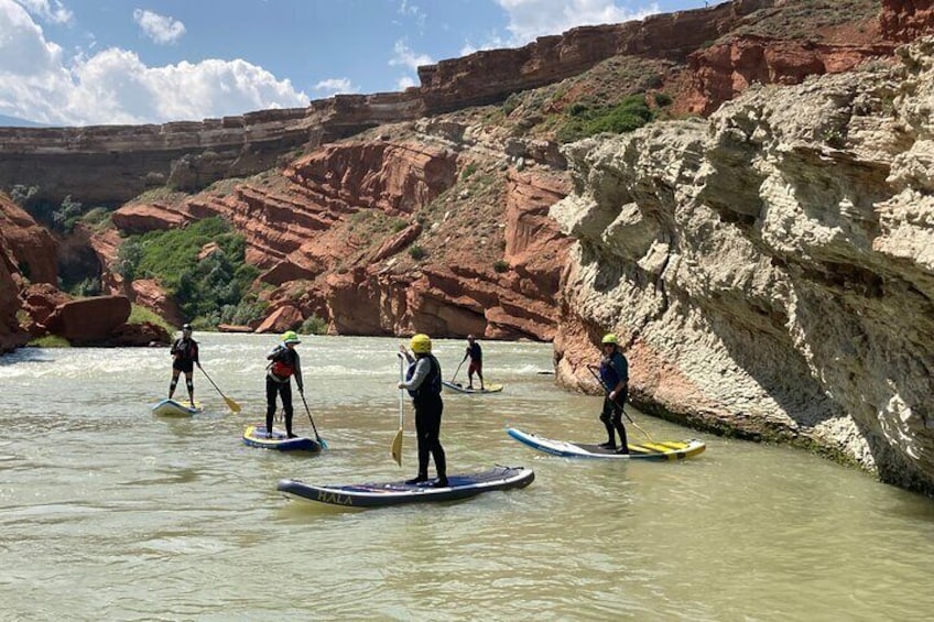 People paddleboarding on a river with red rock cliffs in the background. 2
