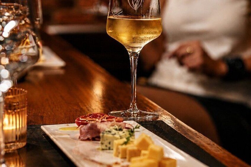 A glass of white wine on a bar counter with a plate of cheese and crackers. 4
