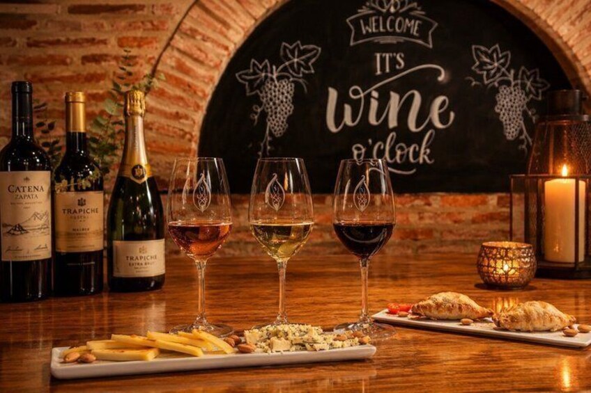 A wine tasting setup with bottles, glasses, and food on a wooden table. 3