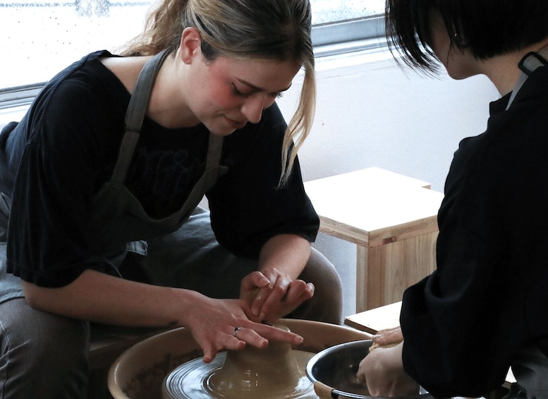 Deux personnes sont en train de travailler la poterie : l’une façonne un pot sur un tour, tandis que l’autre a un bol à portée de main. 2