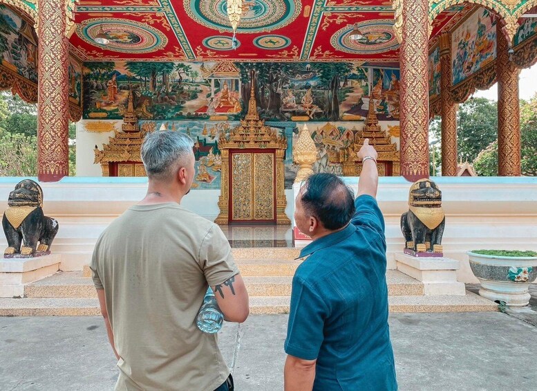Two individuals at a temple with intricate murals and golden statues. 3