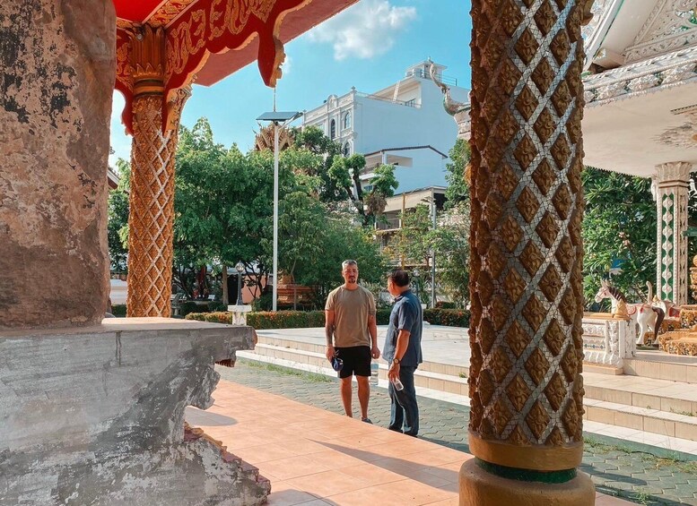 A man and a woman walking past a column with a mosaic pattern, with buildings and trees in the background. 5