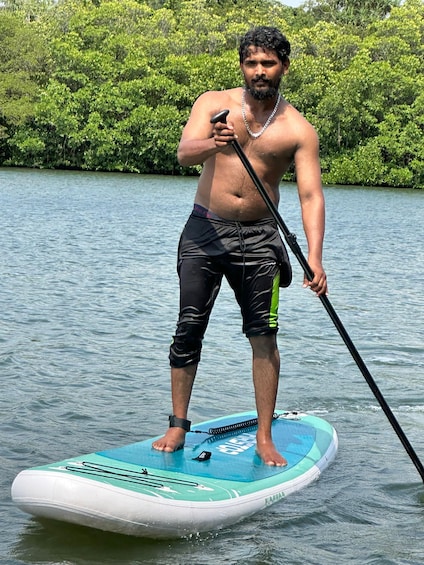 A person paddleboarding on a calm body of water with dense greenery in the background. 1