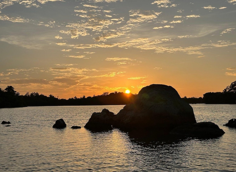 A sunset over a body of water with rocks and a silhouette of trees. 3