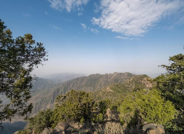 A mountainous landscape with dense green forests and rocky terrain under a clear sky. 3