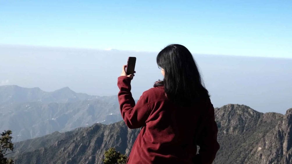 A person taking a photo with a smartphone, overlooking a mountainous landscape. 5
