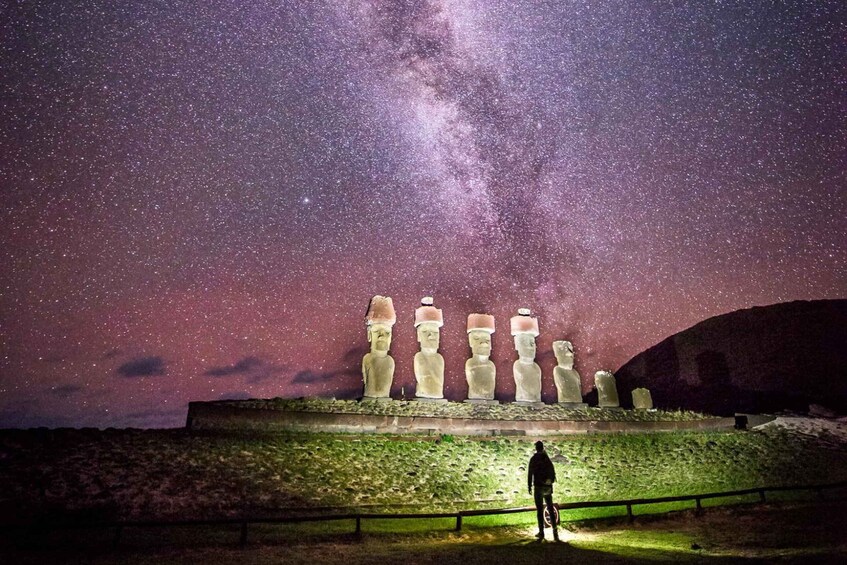 A person standing in front of the Moai statues under a starry night sky. 3