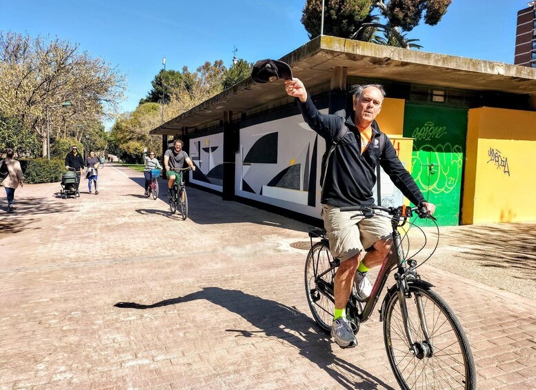 A person on a bicycle with a helmet, another cyclist in the background, and a building with graffiti. 2