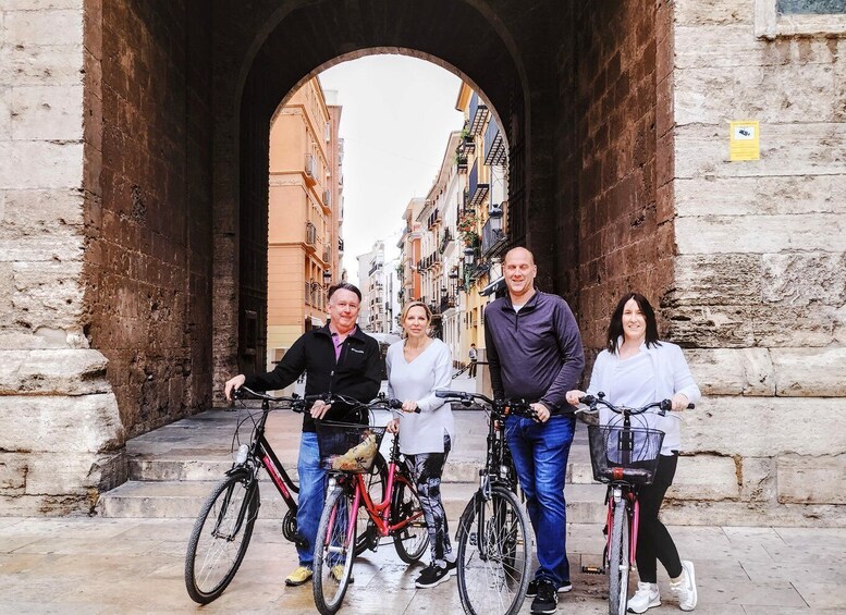 A group of people standing in front of a stone archway with bicycles. 1