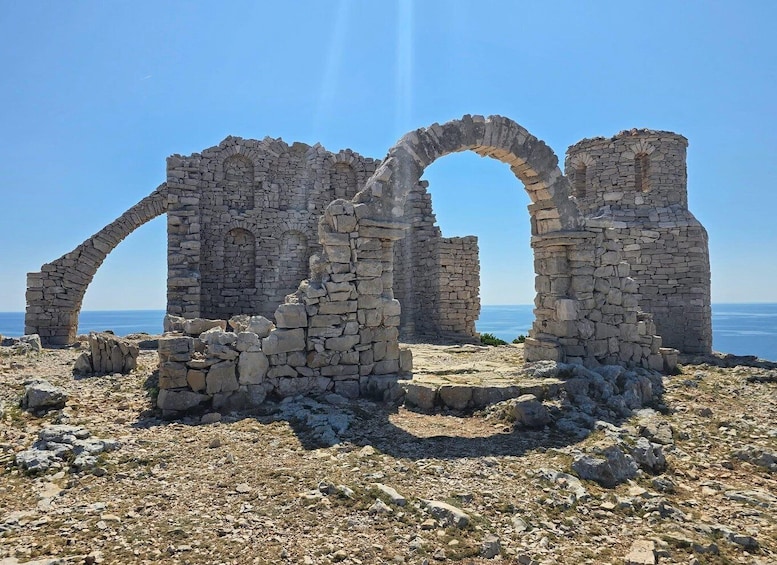 Ancient stone ruins with arches, set against a clear sky and sea backdrop. 3