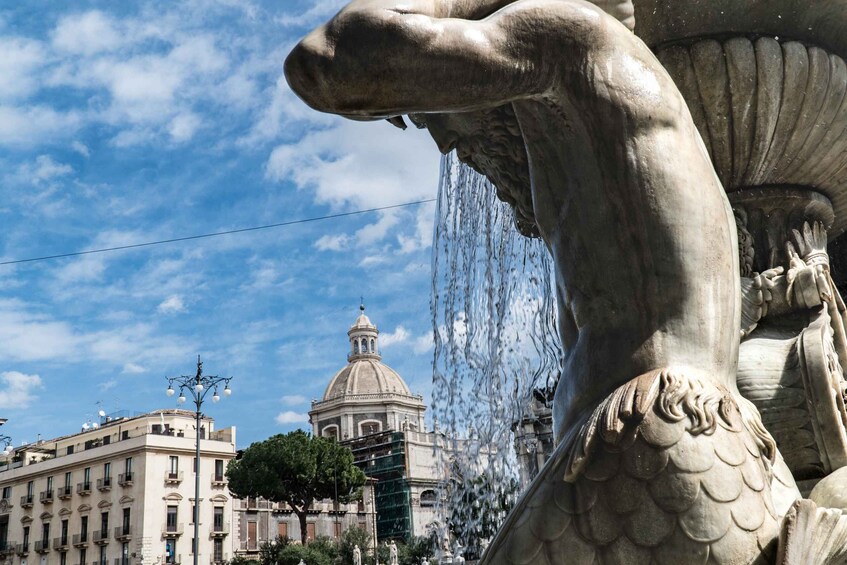 A fountain with a large statue of a hand holding a shell, water flowing from its fingers, and a building with a dome in the background. 1