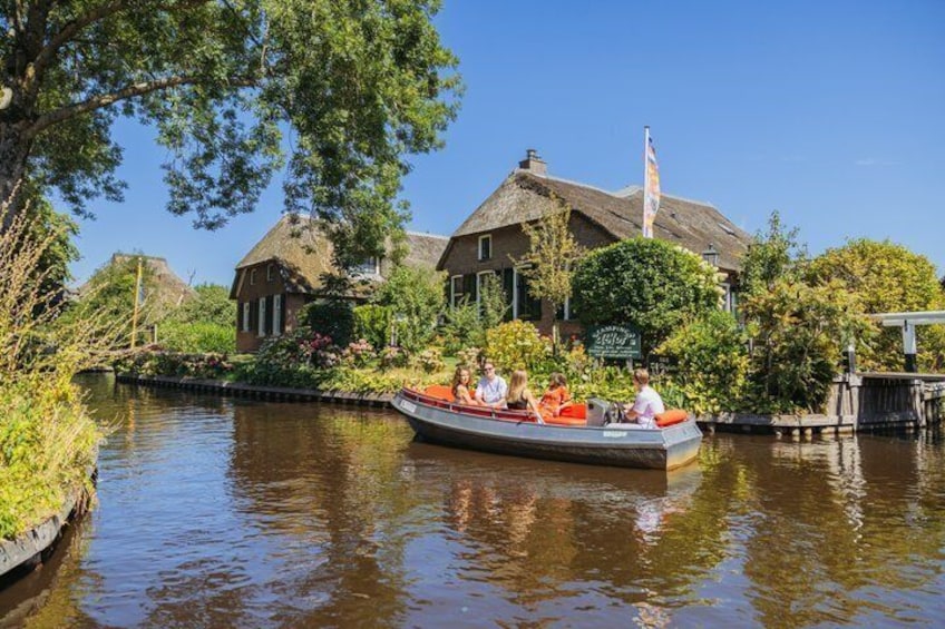 A canal with a boat carrying passengers, a traditional house with a thatched roof, and lush greenery. 2