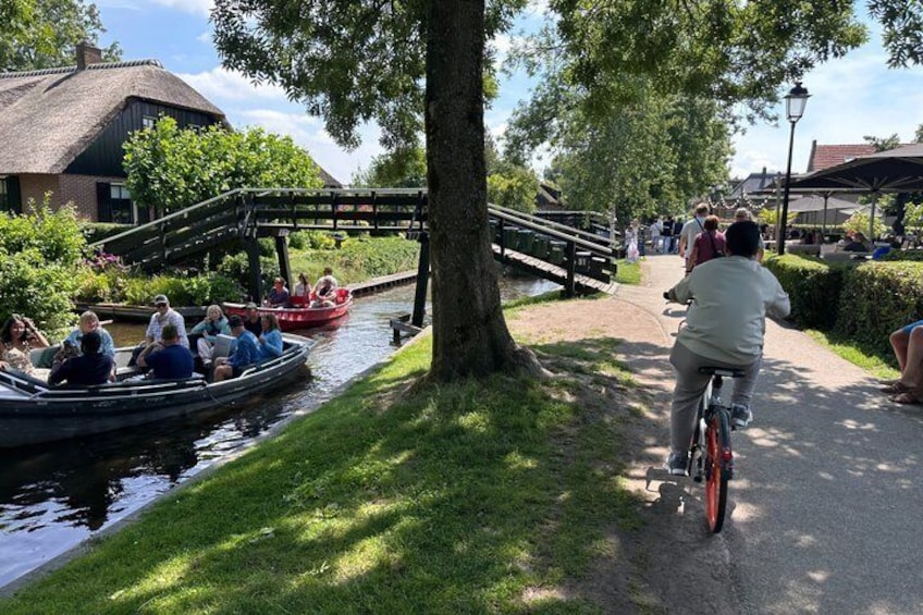 A canal with boats, a bridge, and people cycling and walking. 2