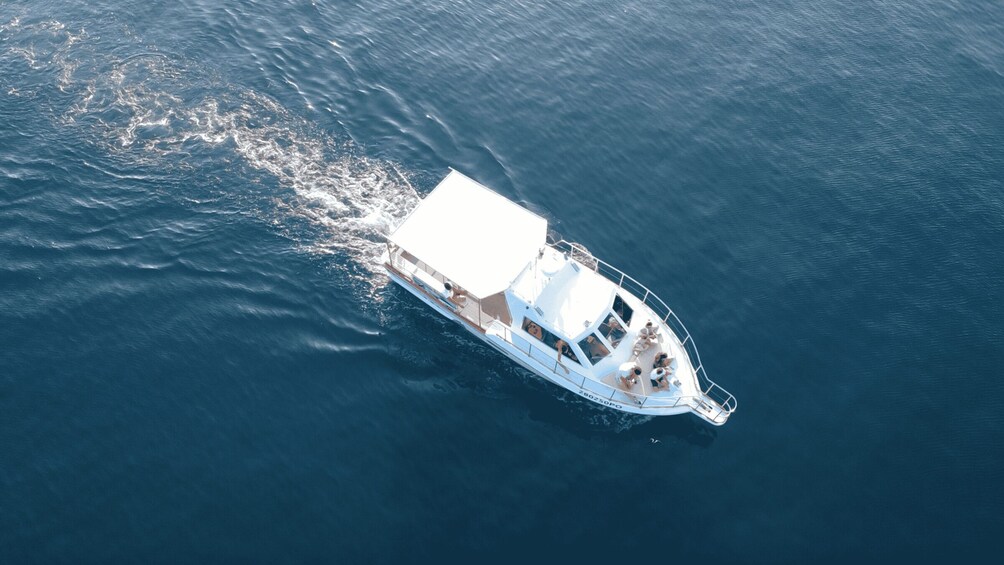 A white boat with a covered deck and a cabin, sailing on a calm blue sea. 1
