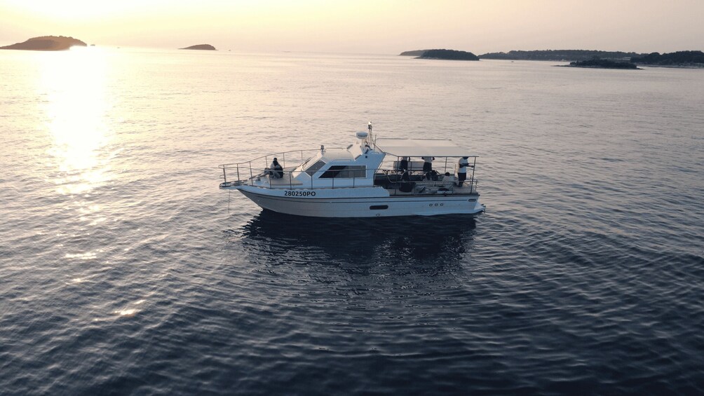 A white boat with the number 280250PO on the side, sailing on calm waters with a sunset in the background. 4