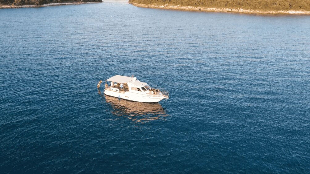 A white boat with a cabin and a covered deck on a calm blue sea. 3