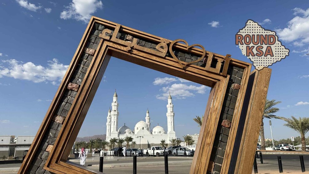 A wooden frame with a sign reading 'ROUND KSA' in front of a mosque with multiple domes and minarets. 4