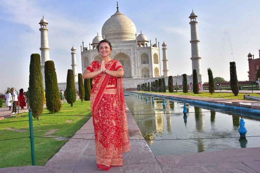 A person in a red traditional outfit standing in front of the Taj Mahal with a reflection in the water. 1