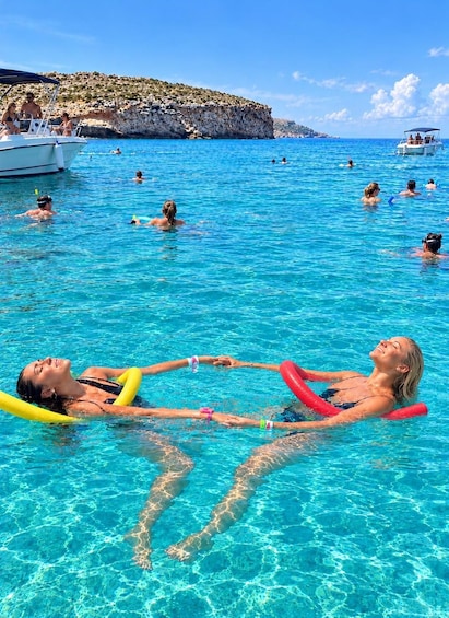 Persone che nuotano in una piscina cristallina blu, con barche e scogliere rocciose sullo sfondo. 5