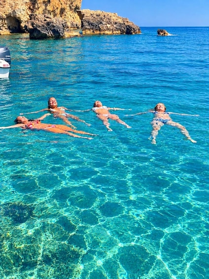 Tre persone che galleggiano in un mare cristallino con alte scogliere rocciose sullo sfondo. 3