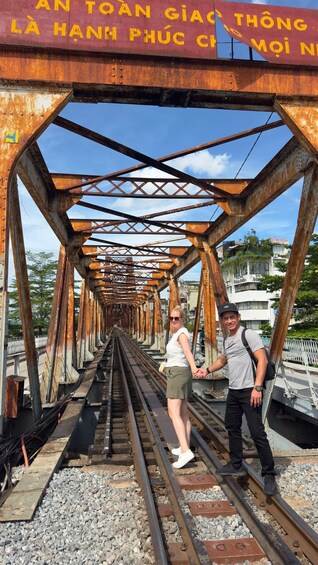 A rusty railway bridge with a couple standing on the tracks. 4