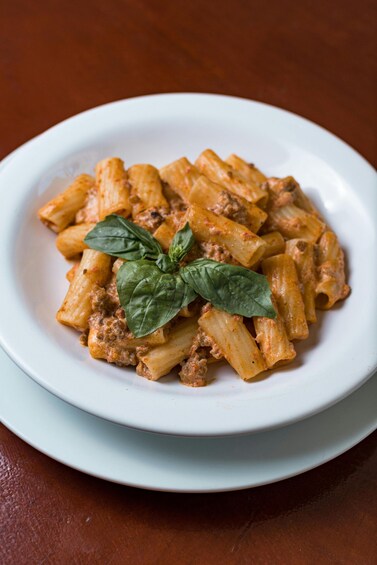 A plate of penne pasta with a meat sauce and basil garnish. 4