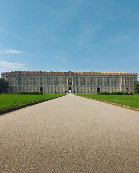 A large, symmetrical building with a central entrance, flanked by manicured lawns and a clear sky. 1