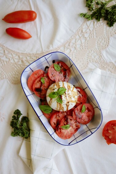 A dish of sliced tomatoes, mozzarella, and basil on a white cloth. 3