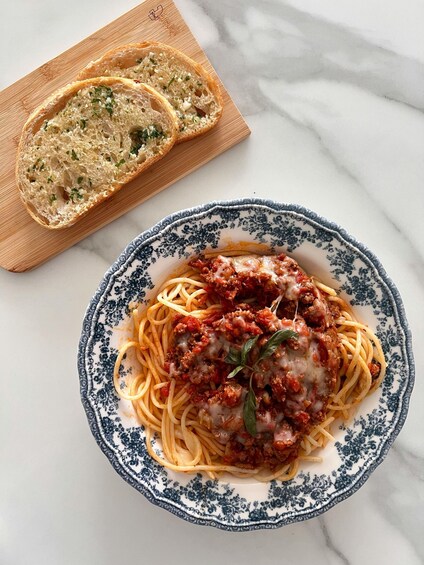 A plate of spaghetti with meat sauce and a slice of bread on a patterned plate. 5
