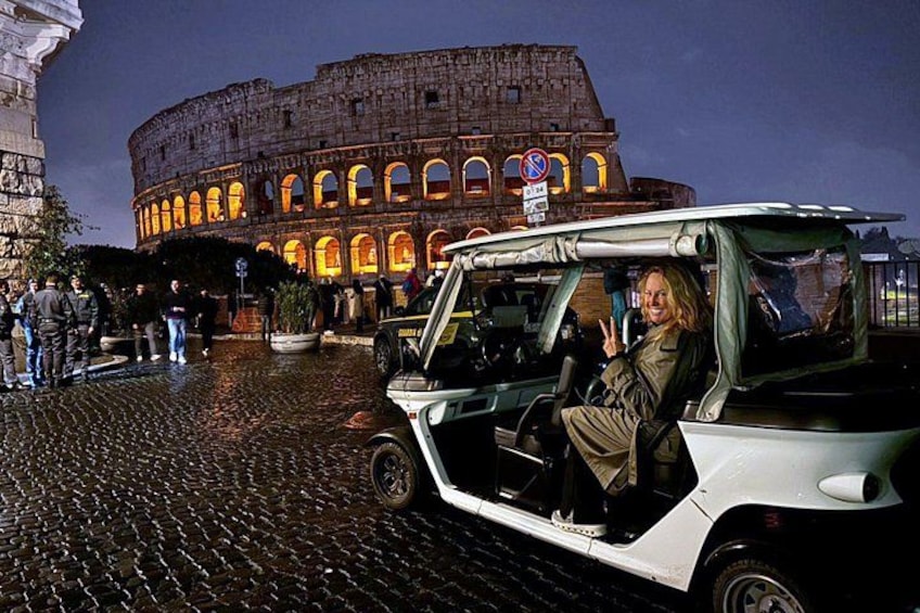 A person in a convertible car with a view of the Colosseum at night. 3