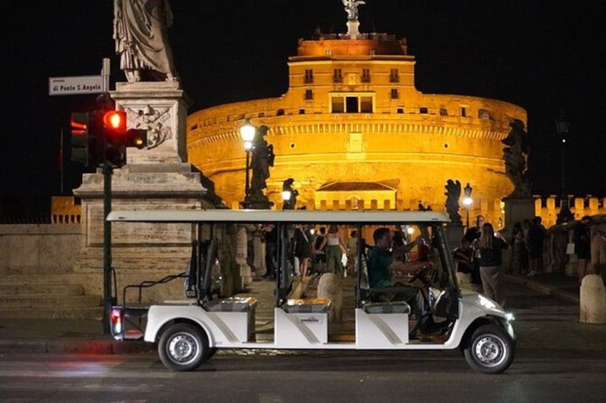 A white golf cart with passengers, a statue, and a large illuminated building in the background. 4