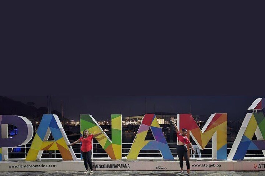 A nighttime view of the Panama City skyline with illuminated letters spelling 'PANAMA' and a person standing in front of them. 2