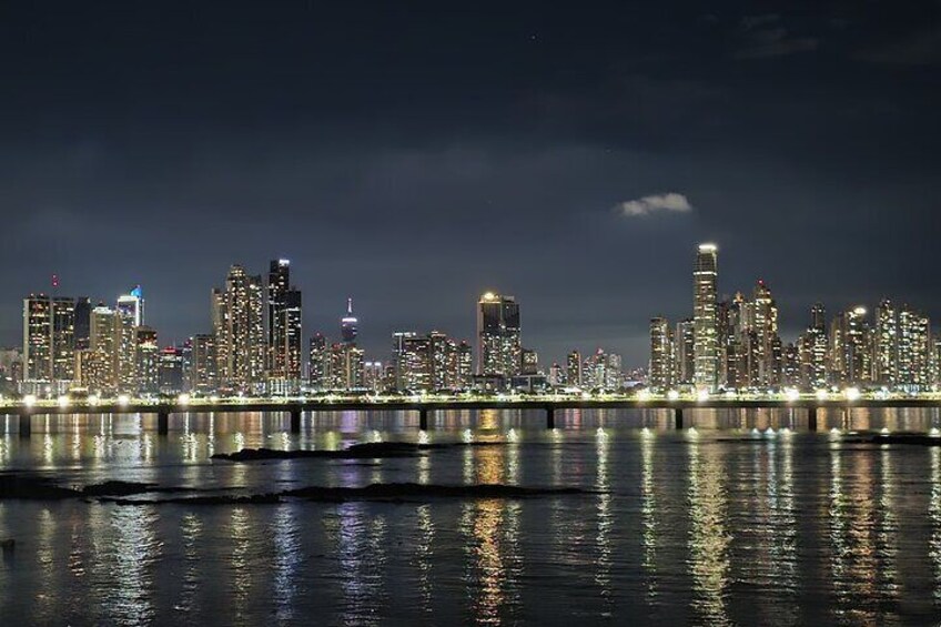 A nighttime city skyline with illuminated buildings reflected in the water. 1