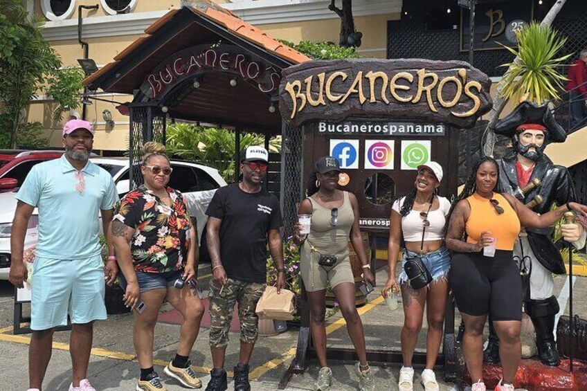 A group of people posing in front of Bucaneros restaurant with a pirate statue. 3