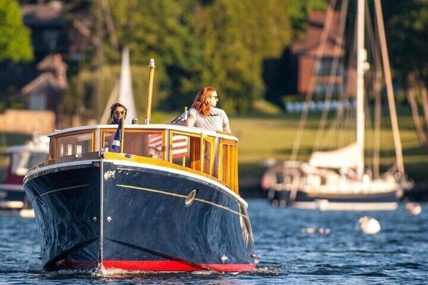 A small boat with two people on board, moving through a body of water with other boats and houses in the background. 3
