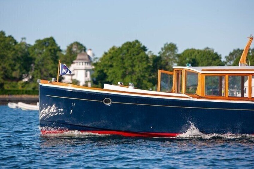 A blue boat with a white cabin and red trim, sailing on water with a building and trees in the background. 2