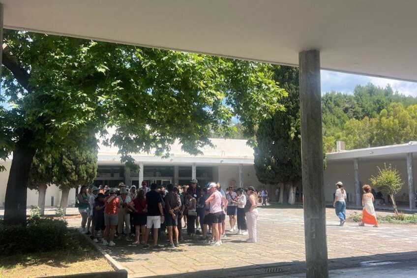 A group of people gathered outdoors under a covered area with trees and a building in the background. 5